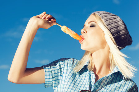 Pretty woman licking an ice cream against  of the blue sky. The girl in joyful feelings. Outdoors, lifestyle.の写真素材