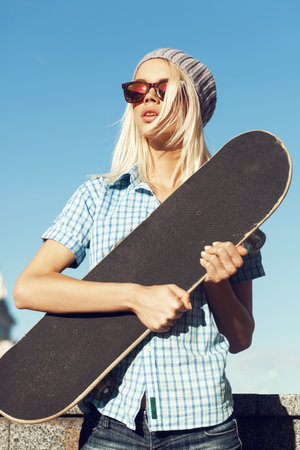 A young girl is standing on the street and holding a skateboard in front of her.  Outdoor lifestyle.の写真素材