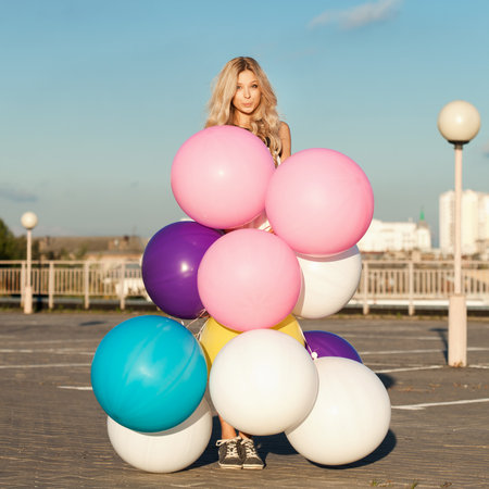 Pretty young woman standing behind big colorful latex balloons. Outdoors, lifestyleの写真素材