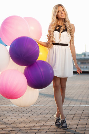 Happy young girl with big colorful latex balloons against the evening sun going down. Beauty Romantic Girl Outdoors.の写真素材
