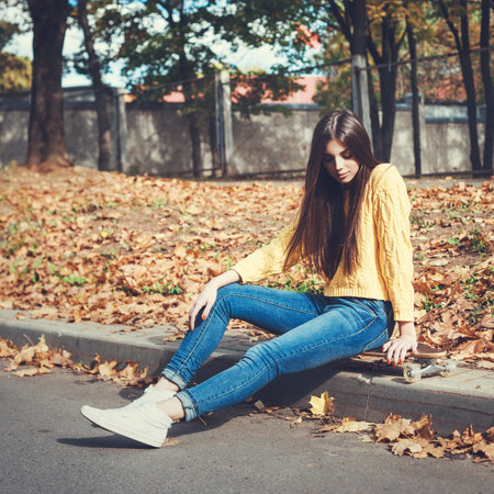 Beautiful young girl sitting on longboard in the afternoon. Skateboarding. Outdoors, lifestyleの写真素材