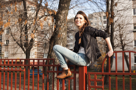 Portrait of a beautiful girl hipster. Naughty young woman sitting on the fence. Outdoors, lifestyle.の写真素材
