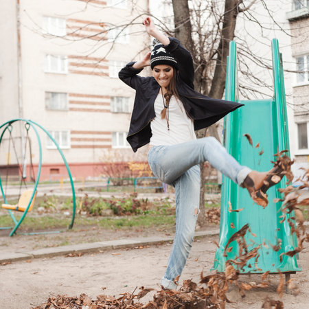 Portrait of a beautiful happy girl hipster kicking leaves. Outdoors.の写真素材