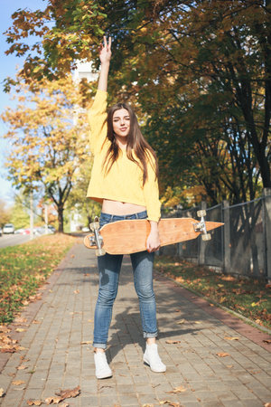 Beautiful young woman in yellow pullover having fun with a longboard in the afternoon. Skateboarding. Outdoors, lifestyleの写真素材