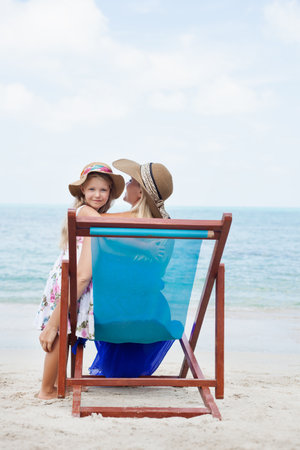 Little beautiful girl embracing her young mother sitting in a chair on sea beach. Outdoorsの写真素材