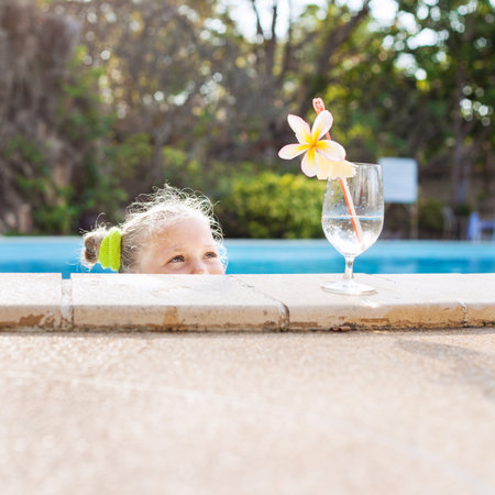 Funky little girl looking to cocktail in tropical beach pool. Outdoorsの写真素材