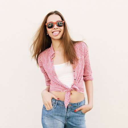 Young woman in sunglasses posing by the wall. Girl sticking her tongue out. Not isolatedの写真素材