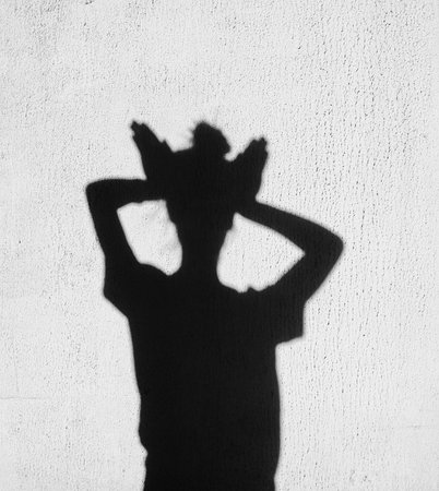 Shadow of girl holding hands on her head around on wall backgroundの写真素材