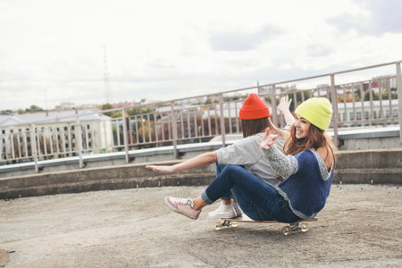 Two young  girl friends sitting together on longboard and having fun. Downhill, longboarding . Outdoors, lifestyle.の写真素材