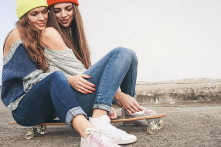 Two young  happy girl friends sitting together on longboard and having fun. Outdoors, lifestyle.の写真素材