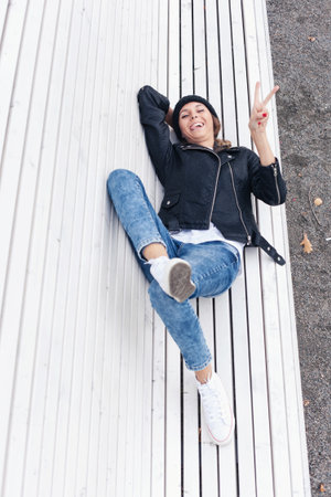 Beautiful young female saluting and winking on a park bench. Outdoor lifestyle portrait of womanの写真素材