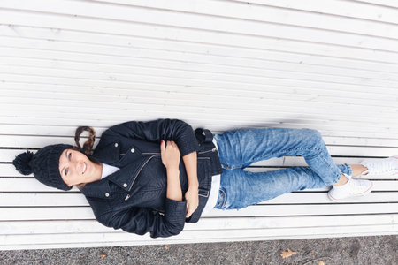 Beautiful young female lying on a park bench. Outdoor lifestyle portrait of woman