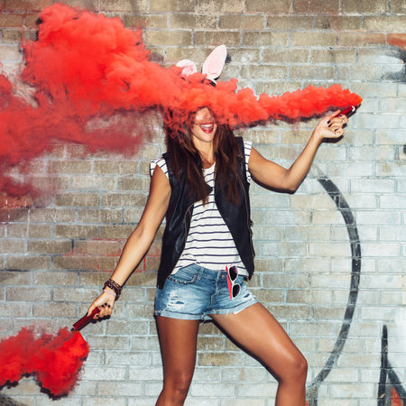 Sexy girl in rabbit ears waving red smoke bombs. Outdoors lifestyle portraitの写真素材
