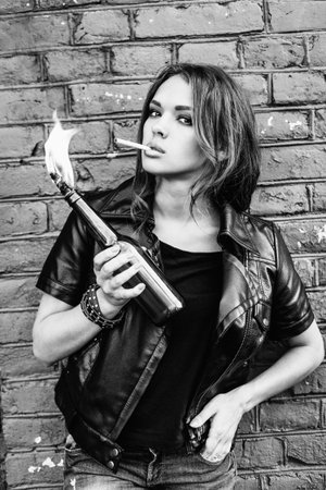 Black and white portrait of a beautiful girl smoking  with a Molotov cocktail in her hand.  Outdoor lifestyle portraitの写真素材