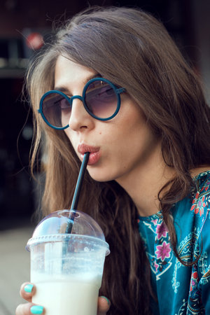 Girl hipster with glasses drinking milk shake. Outdoor lifestyle portrait of womanの写真素材