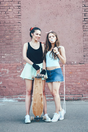 Two young hipster girl friends together having fun with skateboard. Outdoors, lifestyle.の写真素材