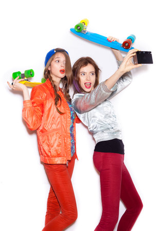 Two young girl friends standing having fun together.  Beautiful women making selfie. Emotion.  Hairstyle. Makeup.  White background, not isolatedの写真素材