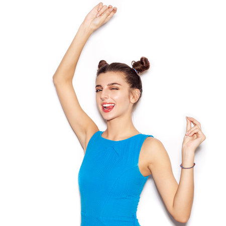 Young woman saluting and winking and showing tongue. Beauty girl with bright makeup hairstyle with horns in a blue dress having fun. On a white background, not isolatedの写真素材