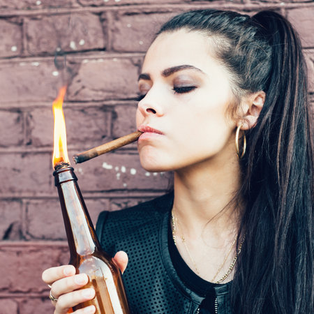 Bad brunette girl lighting up a cigarette from Molotov cocktail bomb in her hand.  Outdoor lifestyle portraitの写真素材