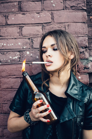 Bully girl lighting up a cigarette from Molotov cocktail bomb in her hand.  Outdoor lifestyle portraitの写真素材