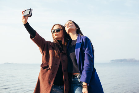 Two funny girlfriends doing selfie on the beach in front of the sea. Outdoor lifestyle portraitの写真素材