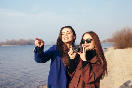 Beautiful young girls taking pictures on the beach in front of the sea. Outdoor lifestyle portraitの写真素材
