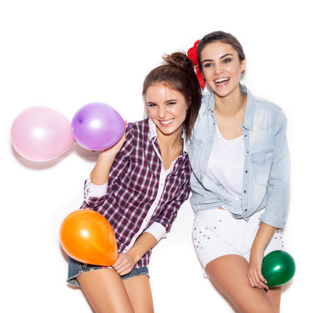 Two happy girls smiling and holding colored balloons. White background not isolatedの写真素材