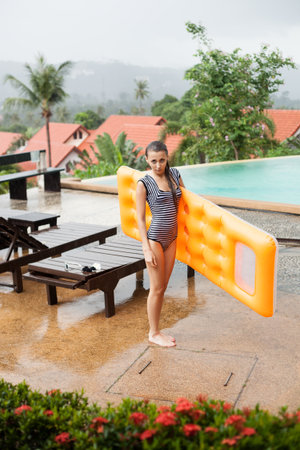 Over head view of an attractive young woman smiling under the rain near swimming pool. outdoors