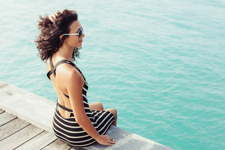 Sexy woman sitting alone on the pier near the sea and looking on the water and waiting for somebody in oceanの写真素材