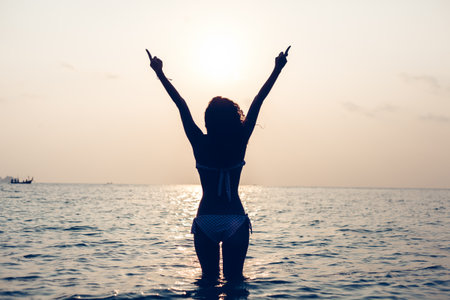 Free woman enjoying freedom feeling happy at beach at sunset. Beautiful serene relaxing woman in pure happiness and elated enjoyment with arms raised outstretched up. Latin Caucasian female model.の写真素材