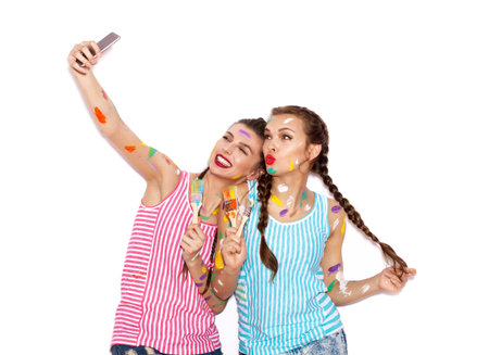 Lovely girl friends having fun. Women with paintbrush taking selfie. White background not isolatedの写真素材
