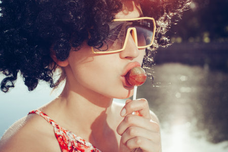 girl with black wig hair sucks lollipop. Outdoors lifestyleの写真素材