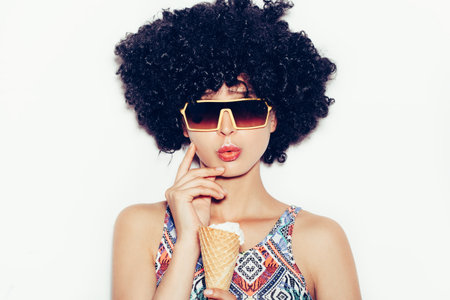 young girl in black wig eating ice cream wearing  sunglasses. White backgroundの写真素材