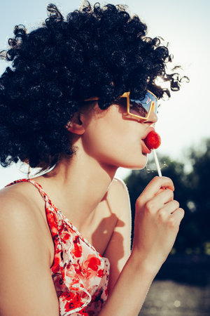 girl with black wig hair sucks lollipop. Outdoors lifestyleの写真素材