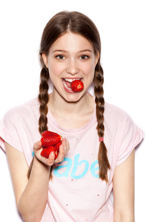 Cute girl holding ripe strawberry. Woman with bright makeup and hairstyle with pigtails. White background not isolatedの写真素材