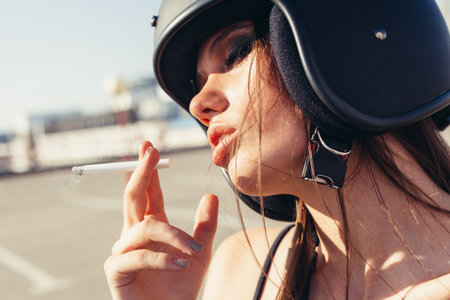 Beautiful woman in motorcycle helmet smoking sigarette. Outdoor lifestyle portraitの写真素材