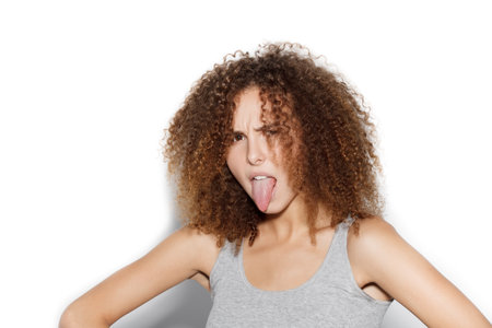 Young happy woman showing tongue. Beauty girl with curly afro hairstyle having fun. On white background not isolatedの写真素材