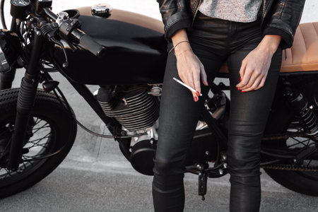 Sexy fashion female biker girl. Young woman sitting on vintage motorcycle and smoking cigarette. Outdoors lifestyle portraitの写真素材
