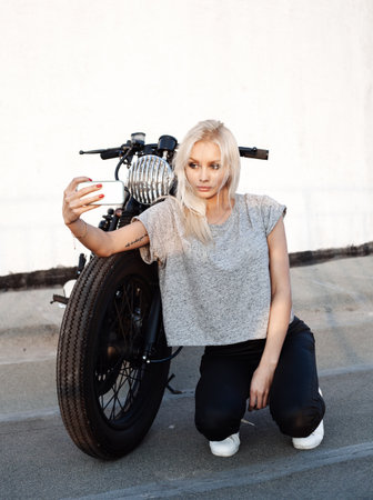 Sexy fashion female biker girl taking selfie with vintage custom motorbike. . Young Blonde woman ...