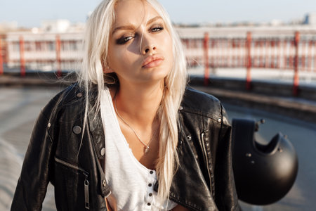 Sexy fashion female biker girl. Blonde woman in leather jacket sitting on vintage custom motorcycle. Outdoors lifestyle portraitの写真素材