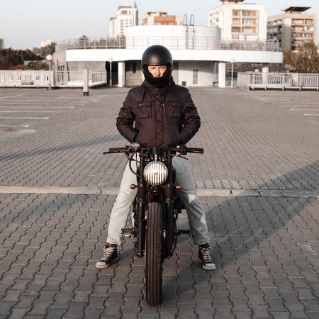 Motorcyclist riding on a motorcycle in the parking lot in the city with open sky on background. Vintage custom motorbikeの写真素材