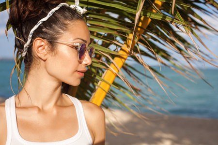 Young female model under palm on sea background. Vacation. Tropics. Fashion shot. Outdoors lifestyle portraitの写真素材