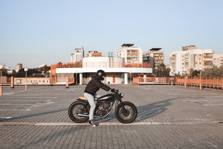Motorcyclist sitting on a bike in the parking lot in the city with open sky on background. Vintage custom motorbikeの写真素材