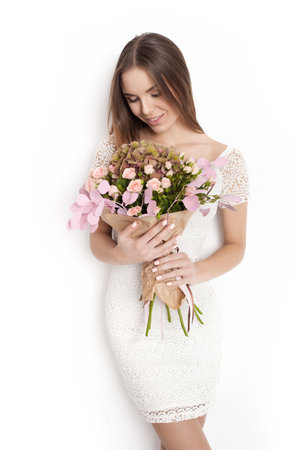 Young cute woman holding a bunch of flowers while standing against white background not isolatedの写真素材