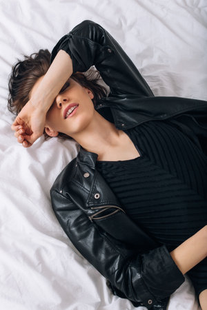 Tired girl covering her face by hand. Young woman wearing a leather jacket and resting in a bed