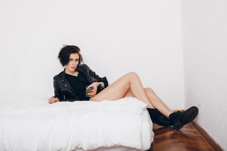 Young woman lying in bed with glass of alcoholの写真素材