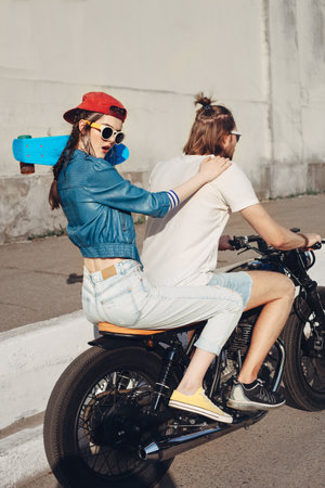 Girl holding skateboard. Young man and woman riding on a sunny day