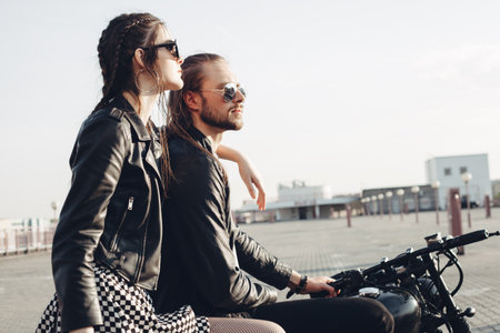 fashion couple sitting on a motorcycle at sunset. young man and woman with vintage custom motorcycleの写真素材