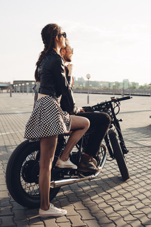 fashion couple sitting on a motorcycle at sunset. young man and woman with vintage custom motorcycle