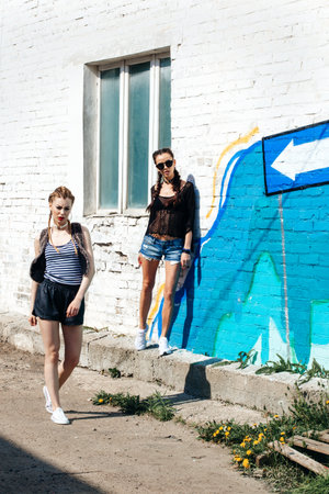 Bright stylish lifestyle outdoor portrait of two pretty best friends girls posing at street. Urban sceneの写真素材